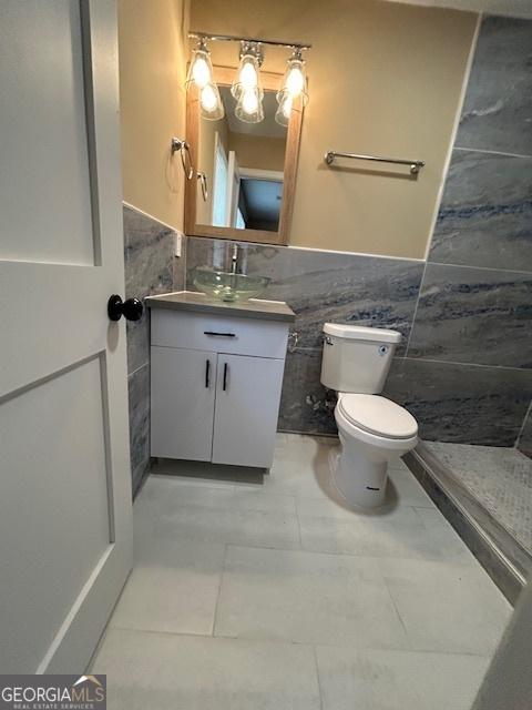 bathroom with vanity, tile walls, toilet, and a wainscoted wall