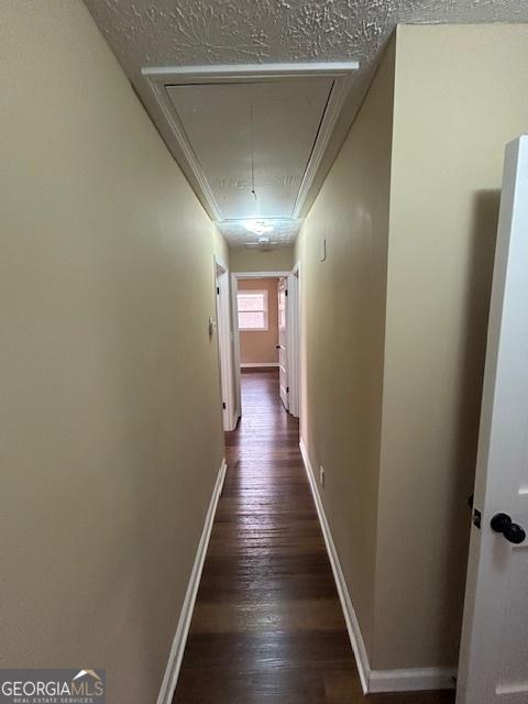 corridor featuring dark wood finished floors, a textured ceiling, attic access, and baseboards