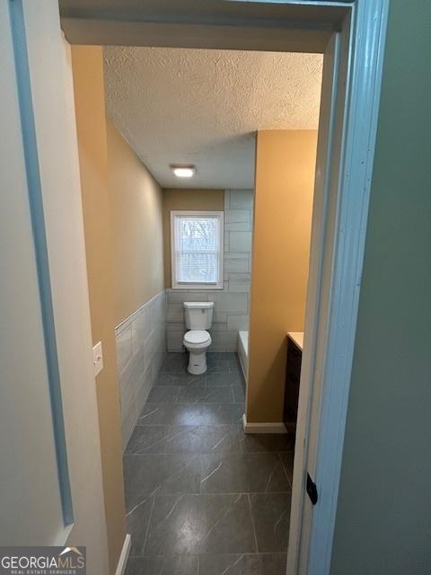 bathroom with toilet, tile walls, vanity, and a textured ceiling