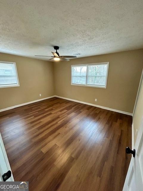 unfurnished bedroom featuring dark wood finished floors, visible vents, a textured ceiling, and baseboards