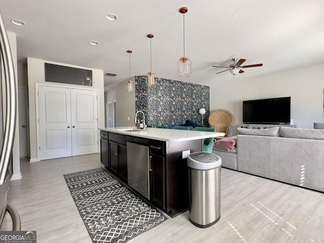 kitchen with a sink, open floor plan, light countertops, dark cabinetry, and dishwasher