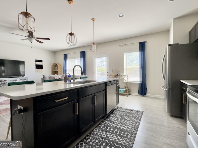 kitchen featuring a center island with sink, appliances with stainless steel finishes, light countertops, dark cabinetry, and a sink