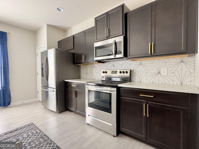 kitchen with light countertops, decorative backsplash, appliances with stainless steel finishes, light wood-style floors, and baseboards