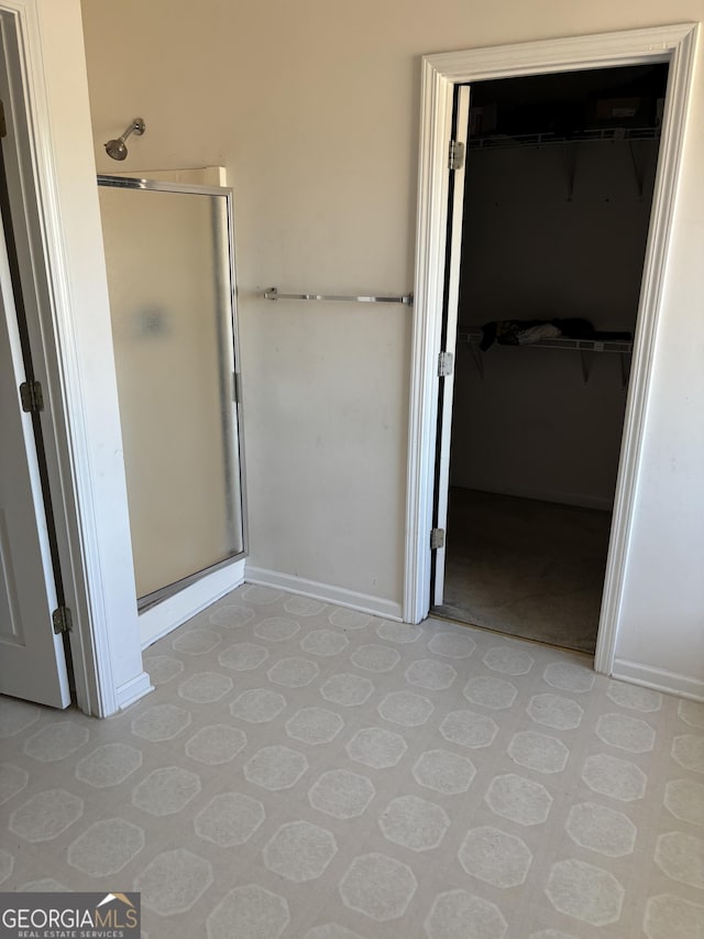 bathroom featuring a spacious closet, a shower stall, baseboards, and tile patterned floors