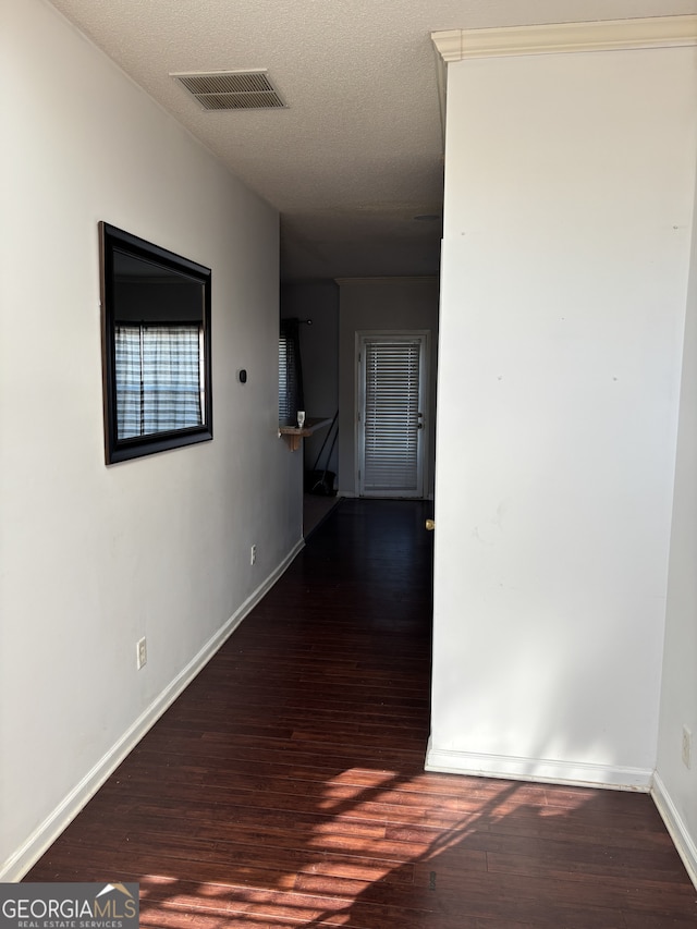 corridor featuring visible vents, a textured ceiling, baseboards, and wood finished floors