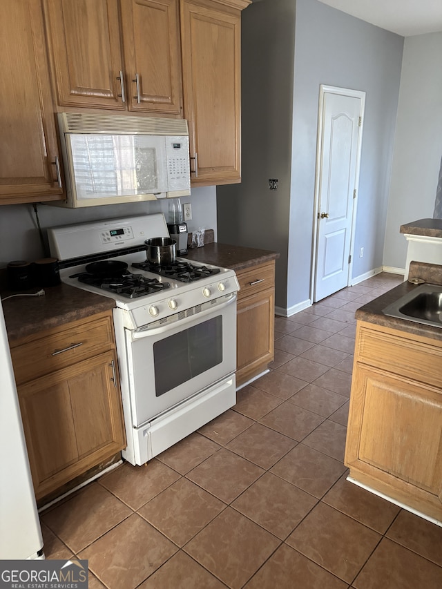 kitchen featuring dark countertops, white appliances, dark tile patterned floors, and baseboards