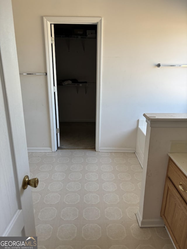 full bathroom featuring a spacious closet, vanity, baseboards, and a bath