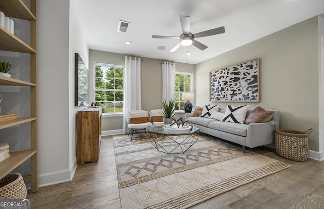 living room featuring a ceiling fan, wood finished floors, visible vents, and baseboards