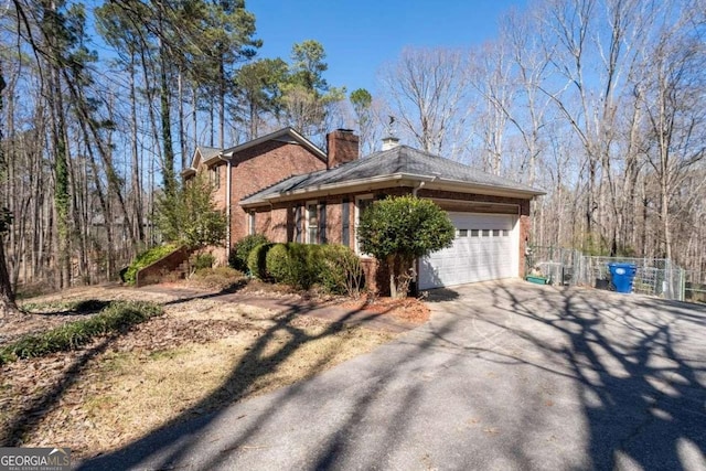 view of side of property with driveway, a chimney, an attached garage, fence, and brick siding