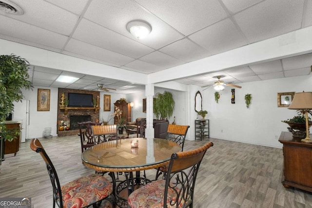 dining room featuring a brick fireplace, a drop ceiling, ceiling fan, and wood finished floors