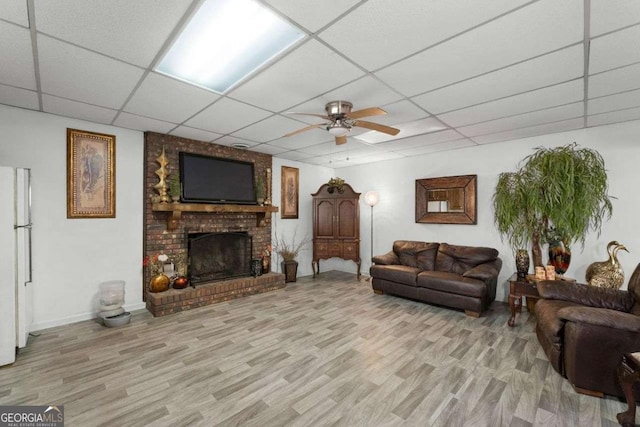 living area featuring a brick fireplace, a ceiling fan, a drop ceiling, and wood finished floors