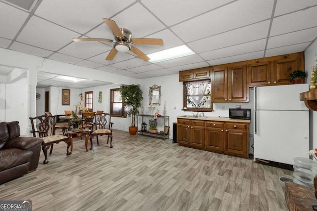 kitchen with brown cabinetry, freestanding refrigerator, light wood-type flooring, black microwave, and a drop ceiling