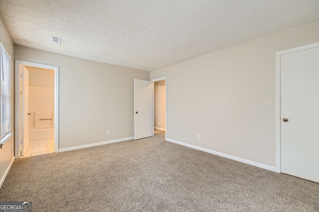 unfurnished bedroom featuring visible vents, ensuite bathroom, carpet flooring, a textured ceiling, and baseboards