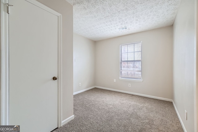 spare room featuring carpet, visible vents, a textured ceiling, and baseboards