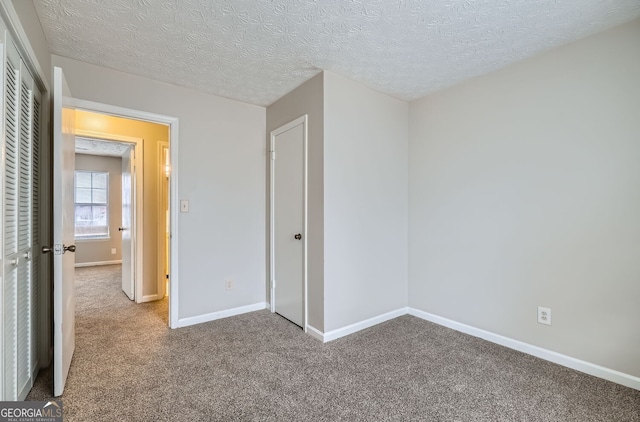 unfurnished bedroom with a textured ceiling, a closet, baseboards, and carpet flooring