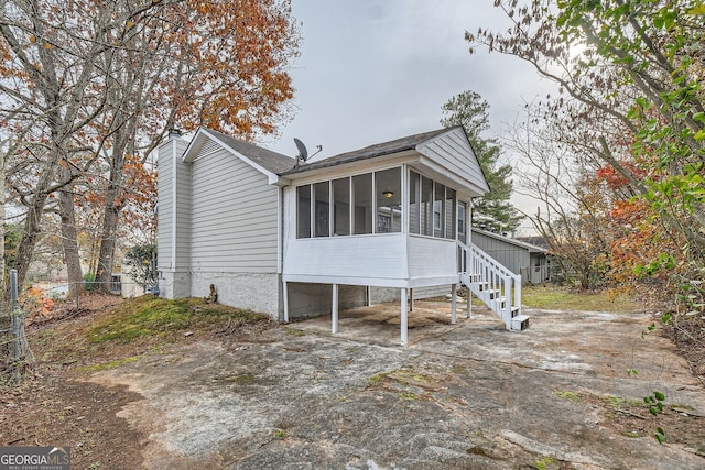 back of property with a chimney, concrete driveway, a sunroom, fence, and stairs