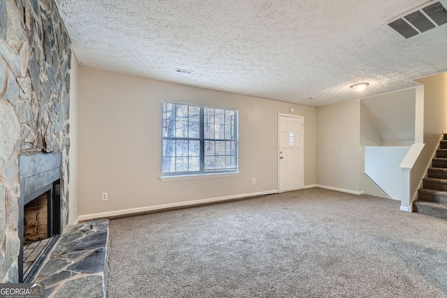 unfurnished living room featuring stairway, visible vents, a stone fireplace, and carpet flooring