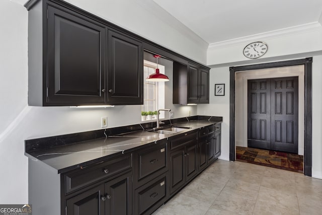 kitchen featuring dark countertops, dark cabinets, hanging light fixtures, crown molding, and a sink