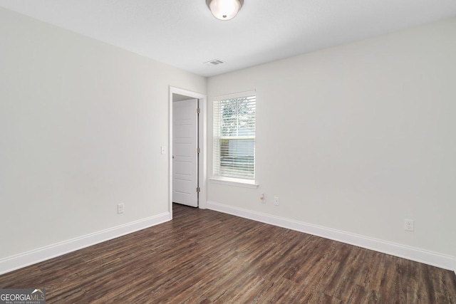 empty room with visible vents, dark wood finished floors, and baseboards