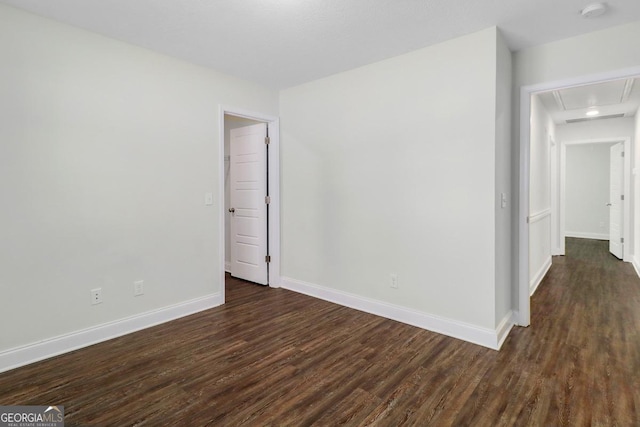 spare room featuring attic access, baseboards, and dark wood-type flooring