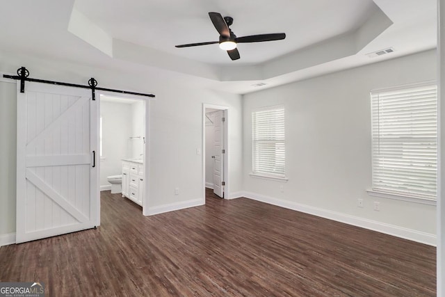 unfurnished bedroom featuring dark wood-style flooring, a raised ceiling, visible vents, a barn door, and baseboards