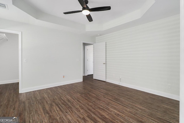 unfurnished bedroom featuring visible vents, baseboards, a spacious closet, dark wood-style floors, and a tray ceiling