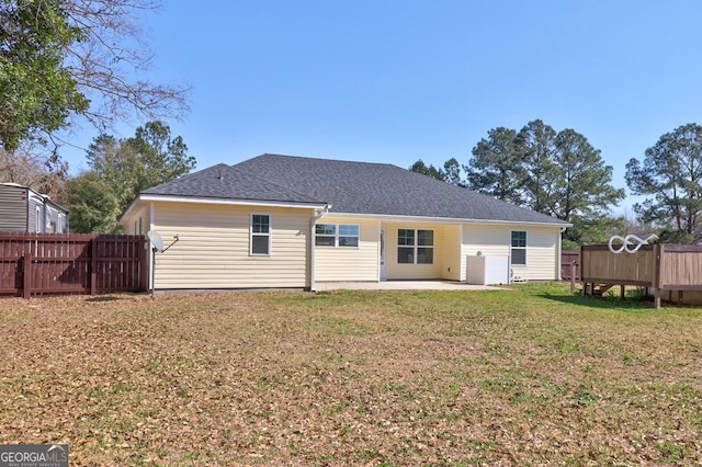 rear view of house with a shingled roof, fence, a patio, and a lawn