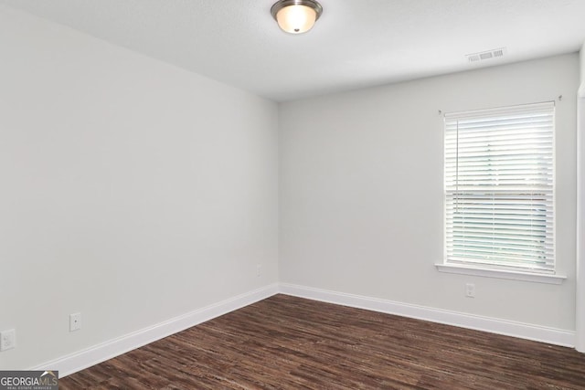 spare room featuring dark wood-type flooring, visible vents, and baseboards