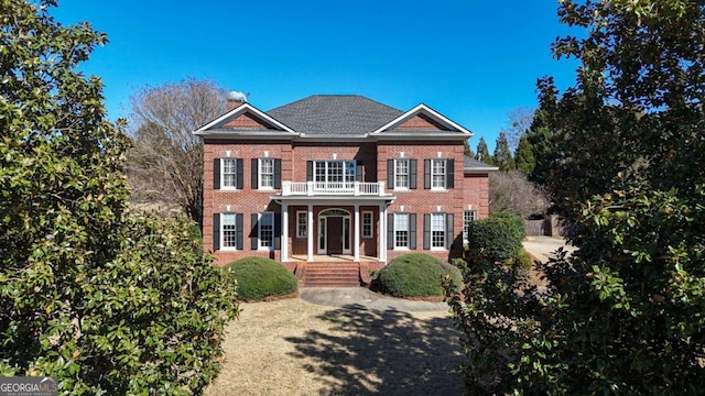 colonial home featuring a balcony, covered porch, a chimney, and brick siding