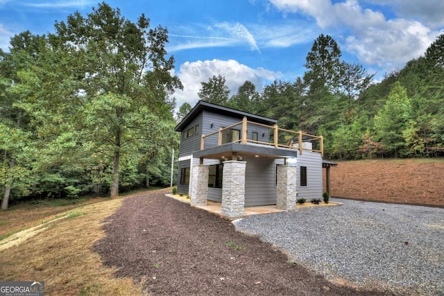 2634 Mountain View Rd, Mccaysville, GA 30555 - view of front of property with gravel driveway, stone siding, a balcony, a forest view, and a patio area