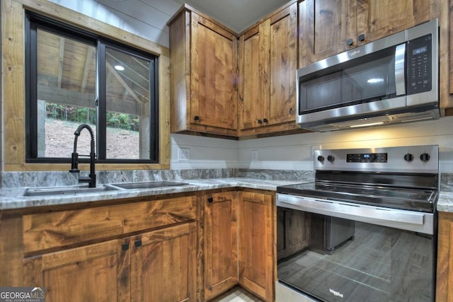 kitchen with appliances with stainless steel finishes, brown cabinets, and a sink