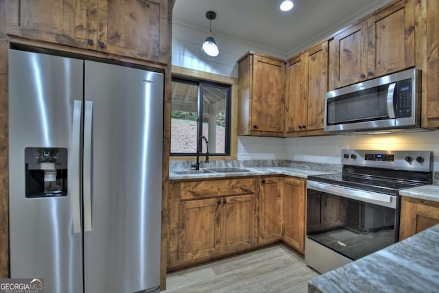 kitchen featuring appliances with stainless steel finishes, brown cabinetry, a sink, and decorative light fixtures