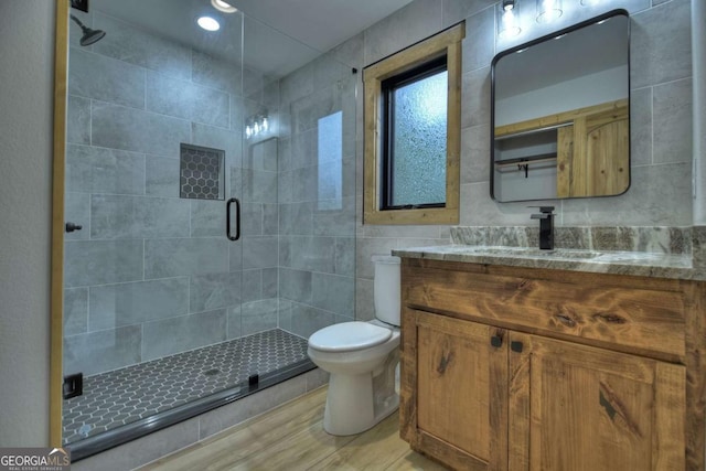 full bathroom featuring a stall shower, toilet, wood finished floors, vanity, and tile walls