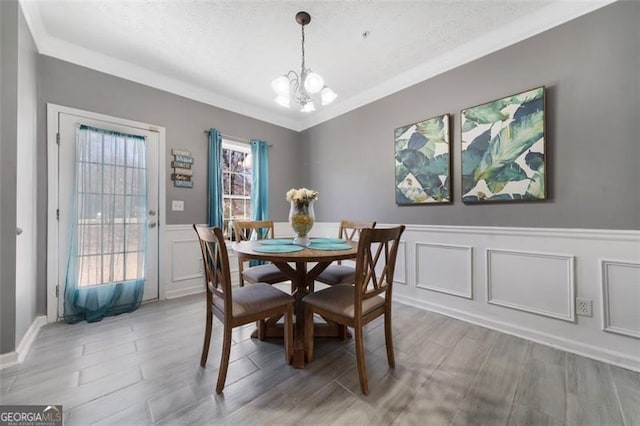 dining room with a chandelier, ornamental molding, light wood-style flooring, and a decorative wall