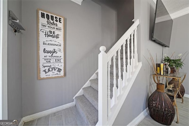 stairway featuring crown molding, a textured ceiling, baseboards, and wood finished floors