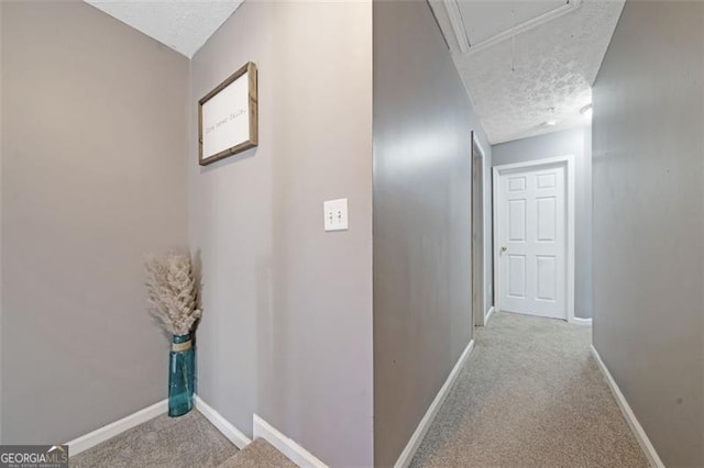 hall featuring a textured ceiling, carpet, attic access, and baseboards