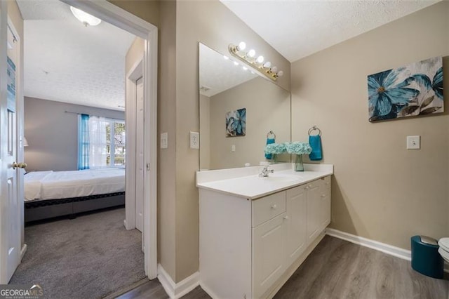 ensuite bathroom with vanity, baseboards, and wood finished floors