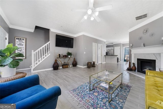 living room with visible vents, baseboards, ornamental molding, stairs, and a high end fireplace