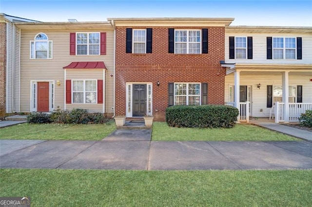 view of property featuring covered porch, brick siding, and a front lawn