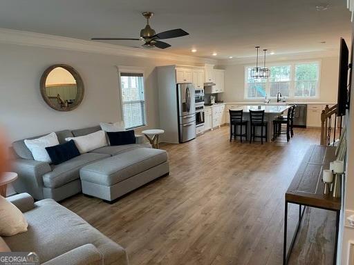 living area featuring light wood-style floors, recessed lighting, a ceiling fan, and crown molding