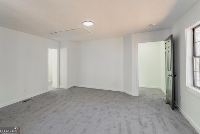 empty room featuring carpet floors, attic access, visible vents, and baseboards