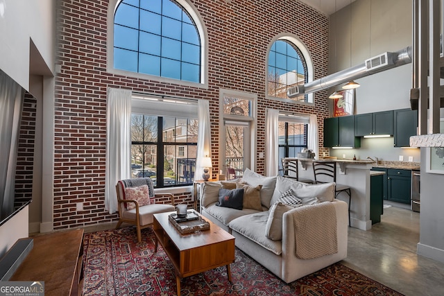 living room featuring brick wall, visible vents, finished concrete flooring, and a towering ceiling