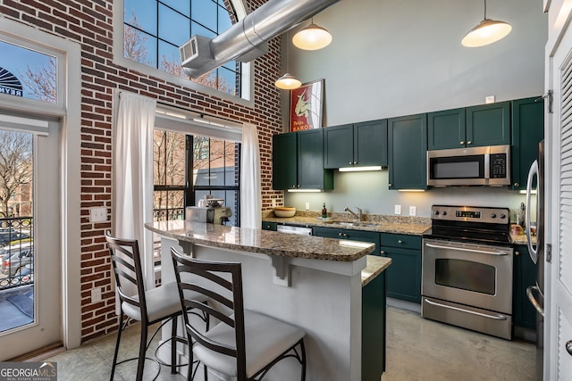 kitchen with appliances with stainless steel finishes, a sink, a high ceiling, and green cabinetry