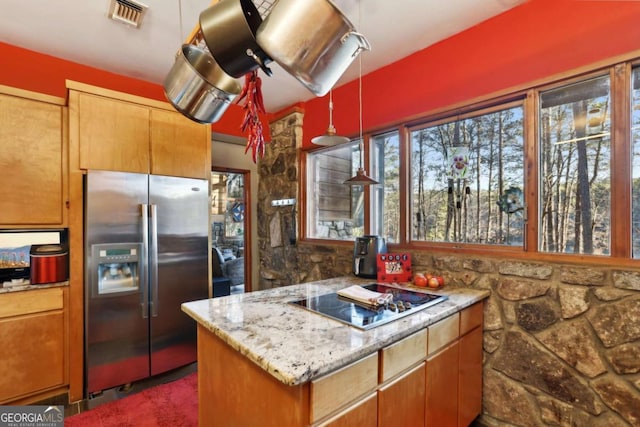 kitchen with light stone counters, black electric stovetop, visible vents, and stainless steel fridge with ice dispenser