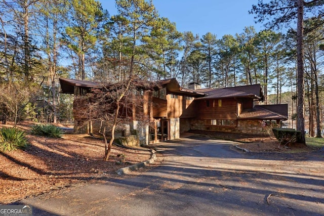 view of front of home with driveway, stone siding, and a chimney