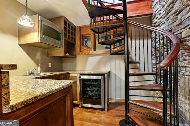 kitchen with wine cooler, stainless steel microwave, light wood-style flooring, a sink, and light stone countertops