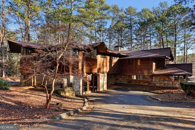 view of front facade featuring aphalt driveway, stone siding, and a chimney