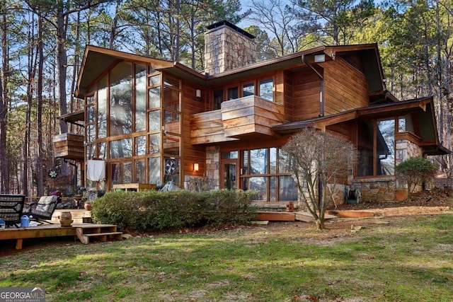 rear view of house featuring stone siding, a sunroom, a lawn, and a chimney