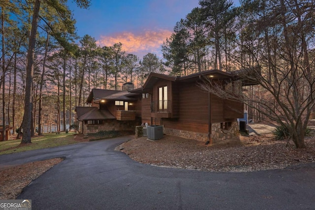 property exterior at dusk with driveway, a chimney, and cooling unit