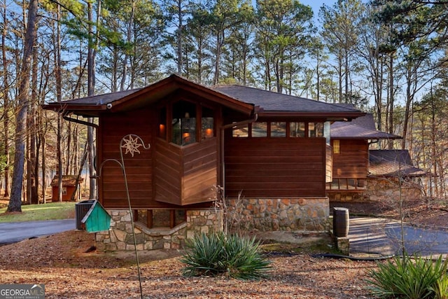 view of side of home featuring stone siding, a shingled roof, and driveway